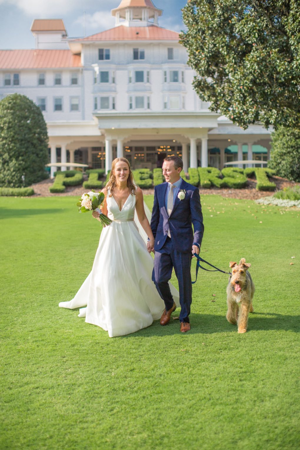 bride and groom with dog on front lawn of the Carolina Hotel in Pinehurst