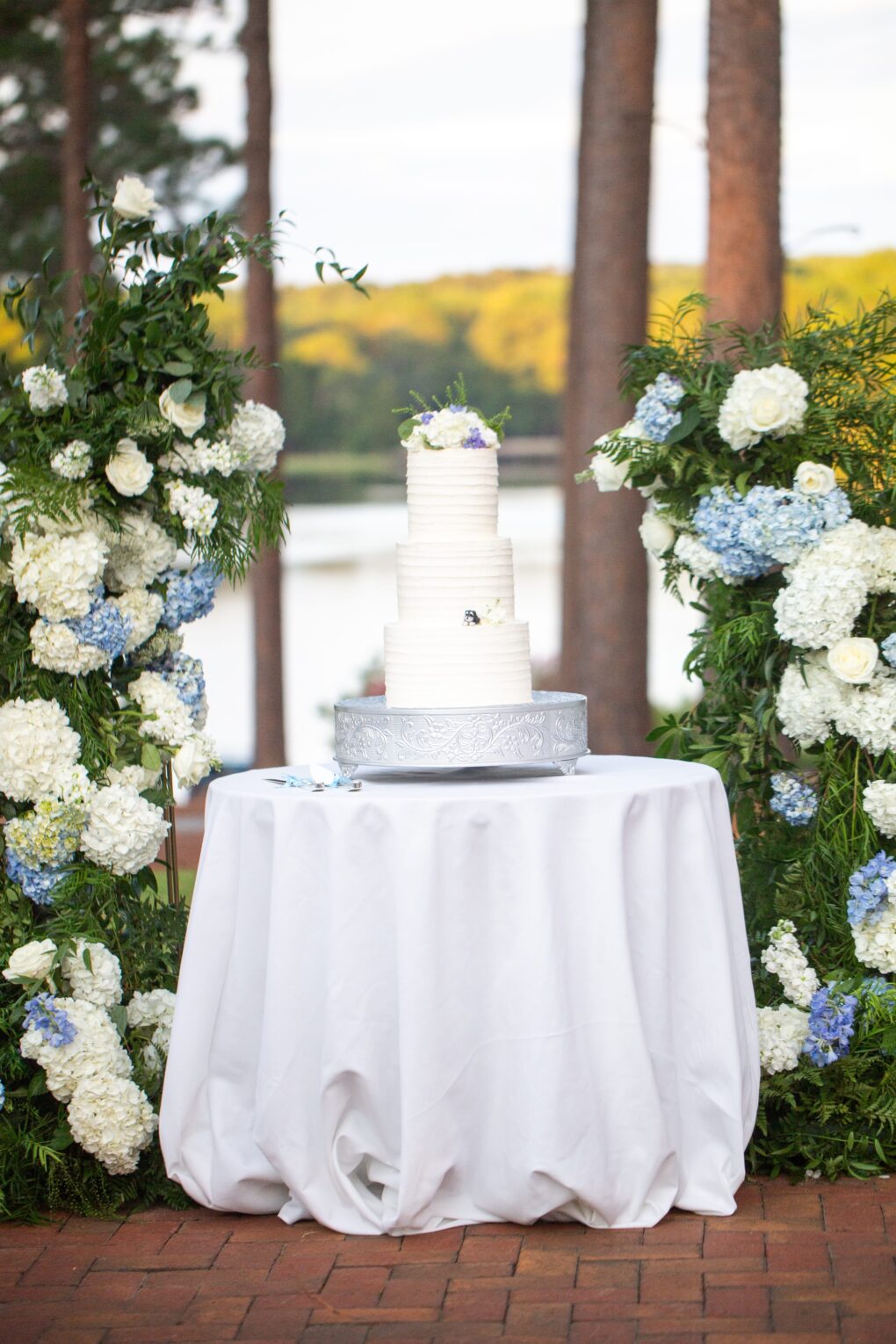 3 tier wedding cake in front of dramatic blue and white flower arch on the back patio at a CCNC wedding