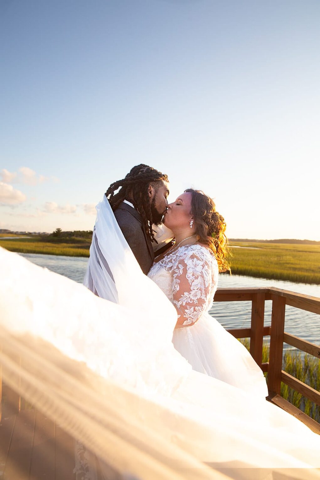 bride and groom kissing on Wrightsville beach pier with veil blowing in wind