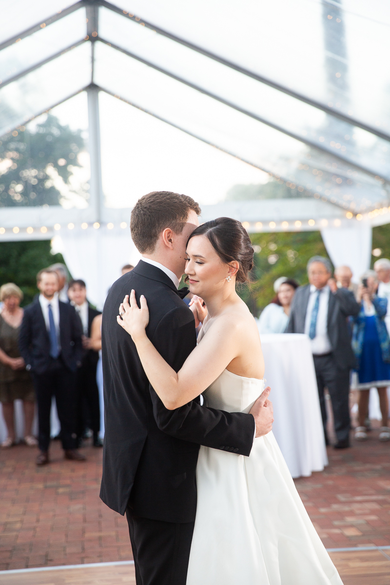 Bride and groom sharing their first dance under a clear tent at a wedding reception.