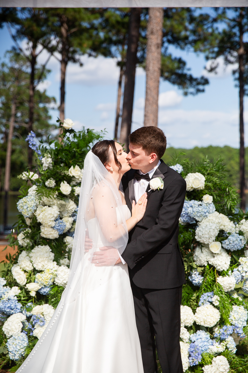 Bride and groom posing under a floral arch in the garden at a Pinehurst wedding.