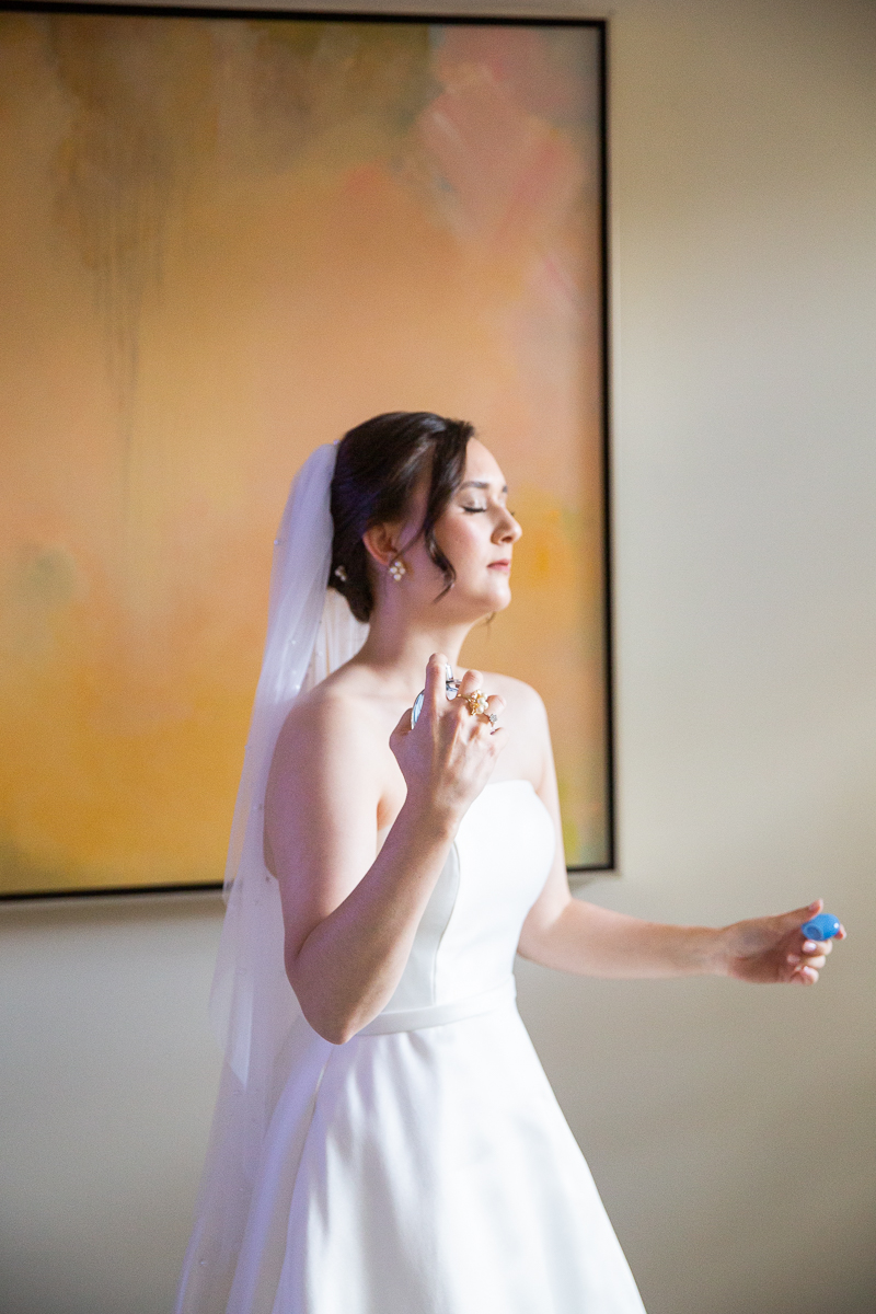 Bride holding a bottle of perfume during wedding preparations at the Country Club of North Carolina.