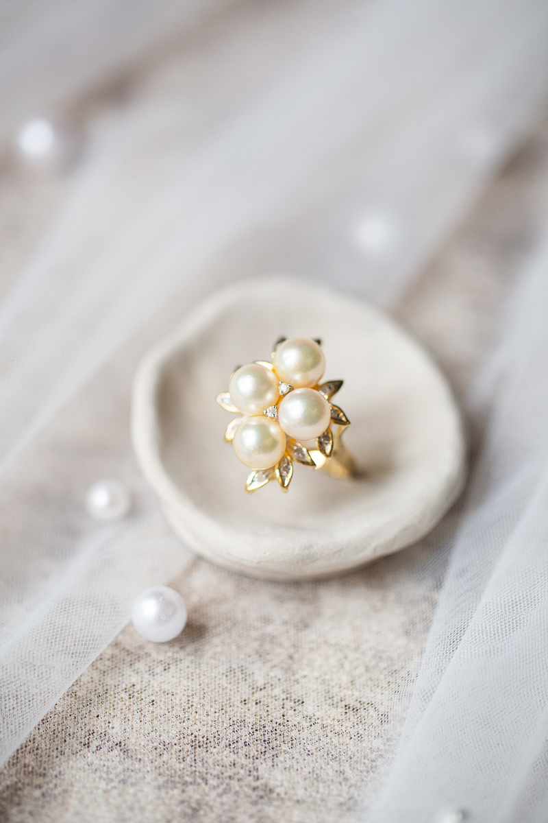 Close-up of a gold engagement ring with pearl accents on a beige dish at a North Carolina wedding.
