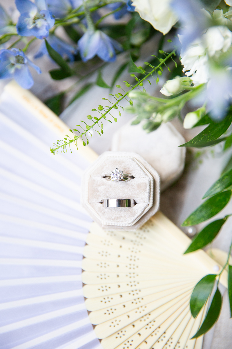 Flat lay of gold wedding details, including a jewelry, fan and florals