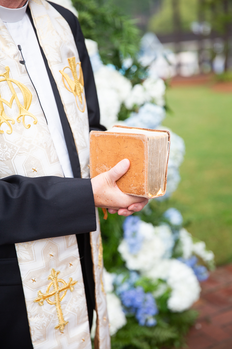 Priest holding a ceremony book during the wedding at a Pinehurst venue.