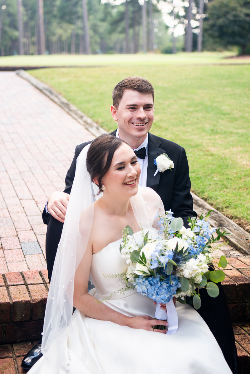 Bride and groom posing on a golf course with a bouquet at a Pinehurst wedding.