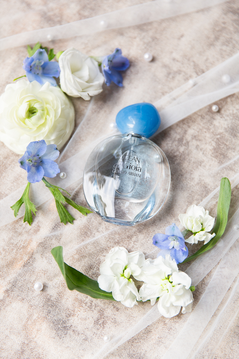 Flat lay of wedding details in blue and white tones, including florals and perfume